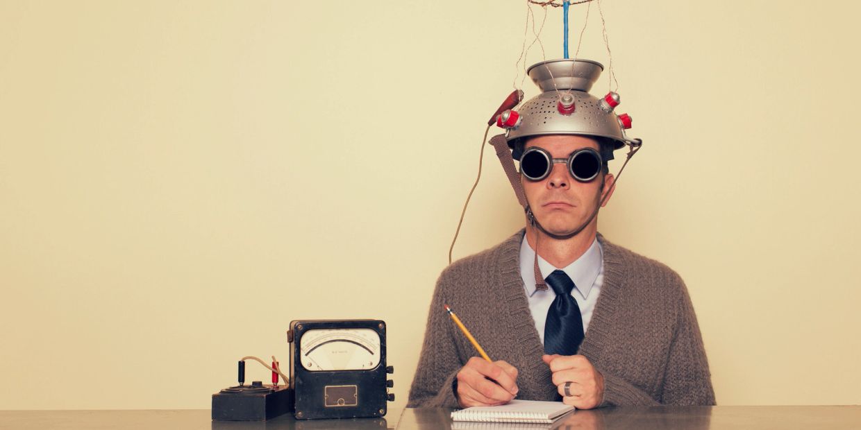 Man wearing a quirky helmet with gadgets, writing in a notebook.