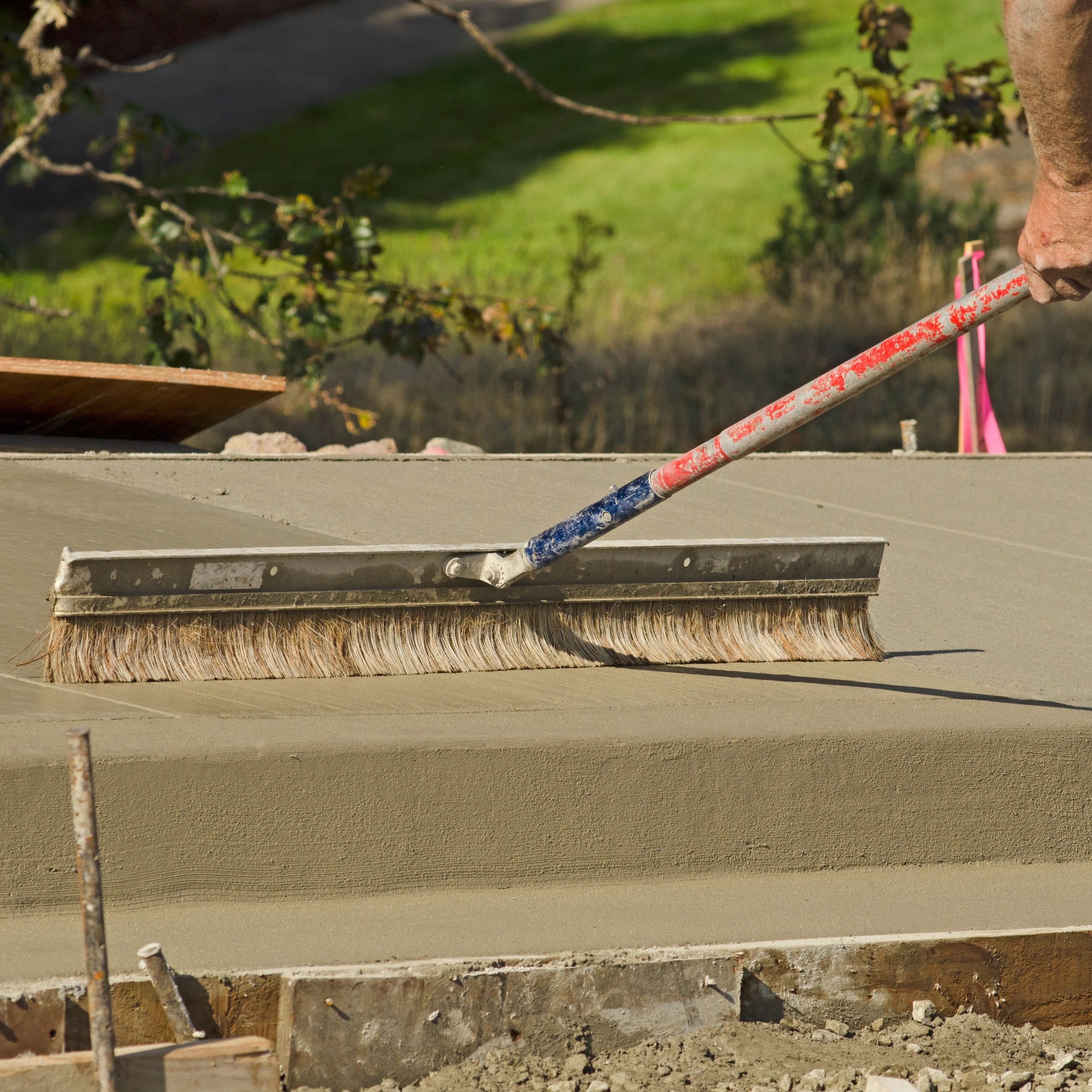 Hand smoothing freshly poured concrete with a broom.