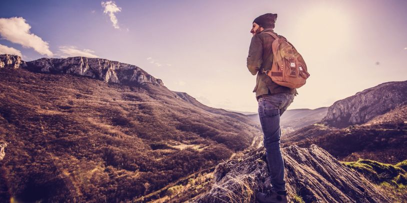 Person with a backpack standing on a rock overlooking mountains.
