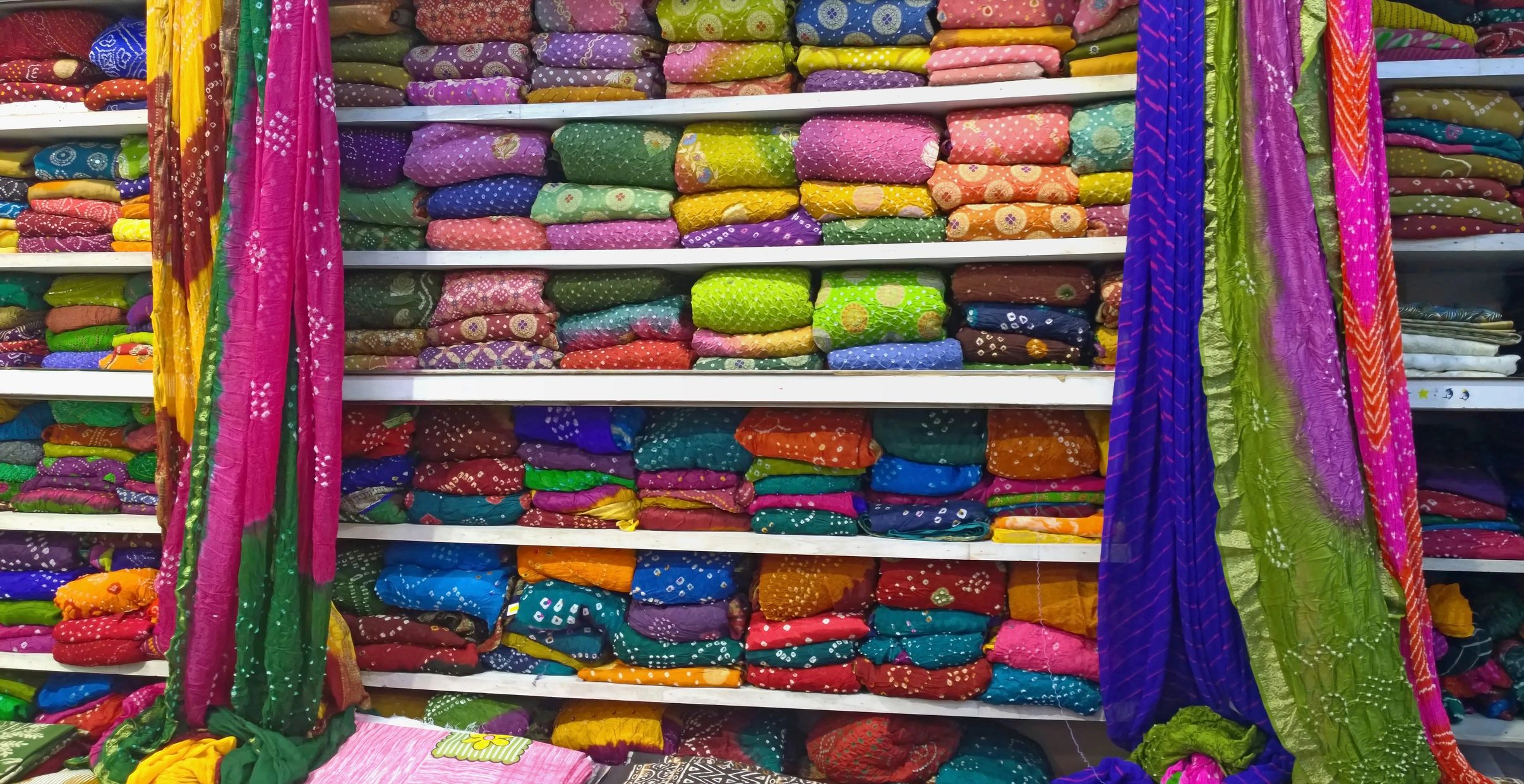 Colorful folded and hanging fabrics on shelves.