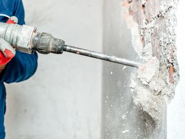 Worker using a jackhammer to break a concrete wall.