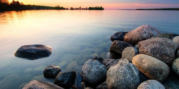 Large rocks along a calm lake shore at sunset with colorful sky.