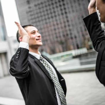 Two businessmen in suits exchanging a high-five outdoors.