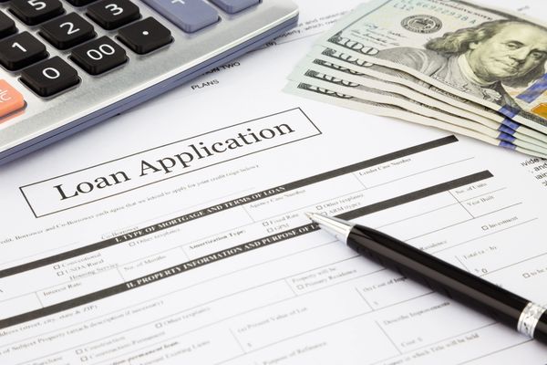 
A pen resting on a Loan Application form, with a calculator and fanned $100 bills nearby.