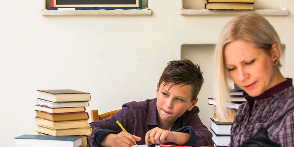 A boy and a woman working with books and writing materials indoors.