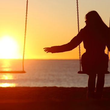 Person on a swing at sunset, reaching for empty swing.