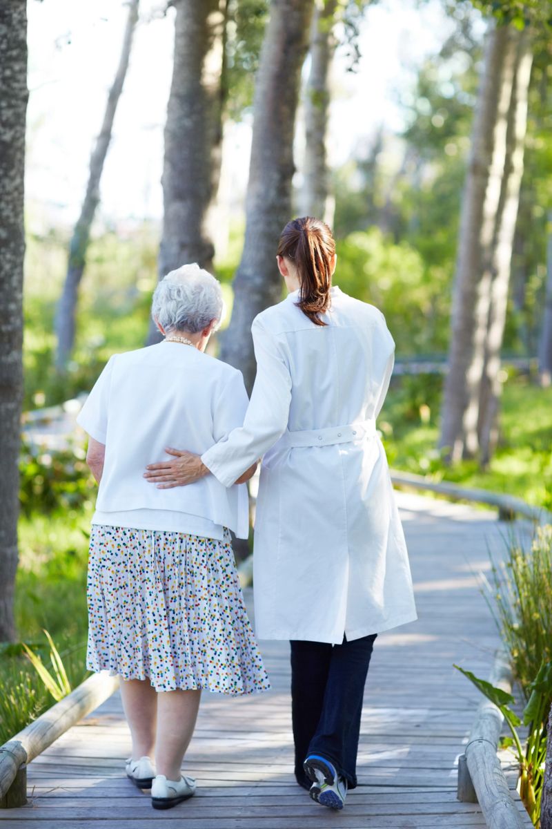A rear view of a caregiver guiding an elderly woman during a stroll through the garden
