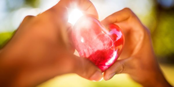 Hands holding a shiny red heart with sunlight shining through.
