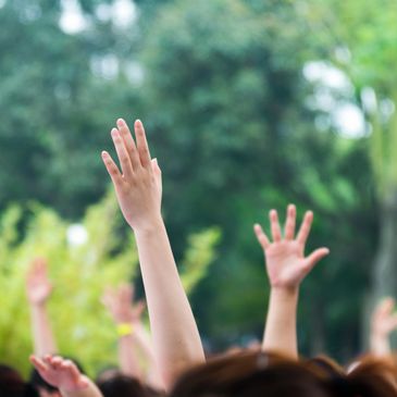Raised hands reaching up in a group outdoors.