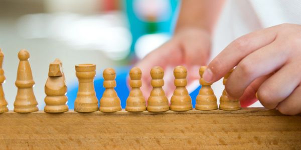 Child arranging wooden chess pieces on a board.