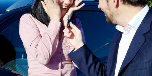 Man handing car keys to excited woman beside a vehicle.