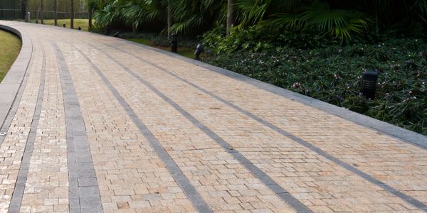 Curved stone pathway lined with trees and lush greenery beside a building.