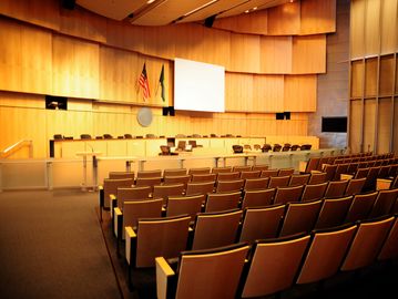 Empty courtroom with rows of seats and a judge's bench.