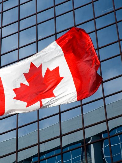 Canadian flag waving in front of a modern glass building.