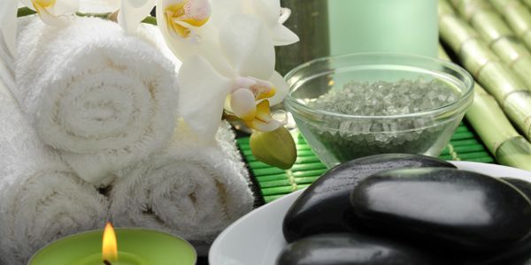 Spa essentials including rolled towels, black stones, and a lit candle.