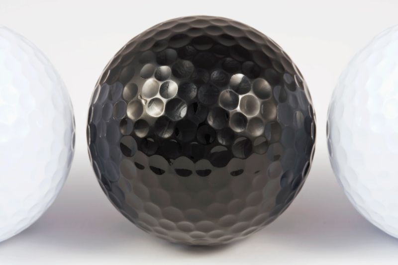 Close-Up of a black golfball between two normal white.