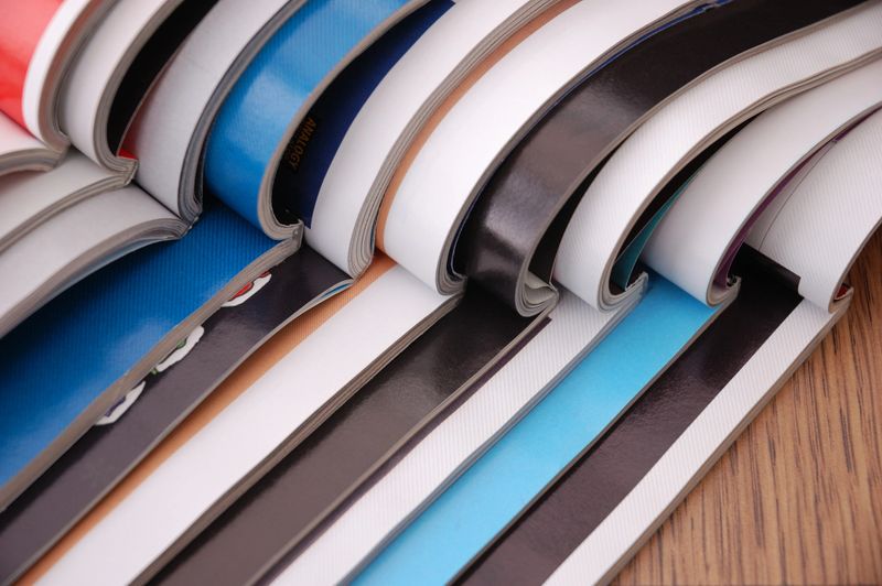 Pile of open magazines on a wooden table.