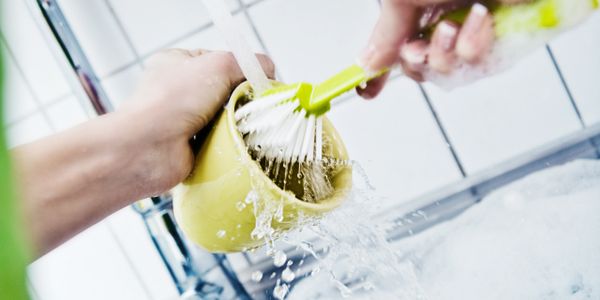 Person scrubbing a yellow cup under running water with a brush.