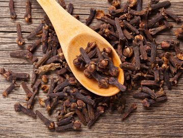 Dried cloves on a wooden spoon and table.