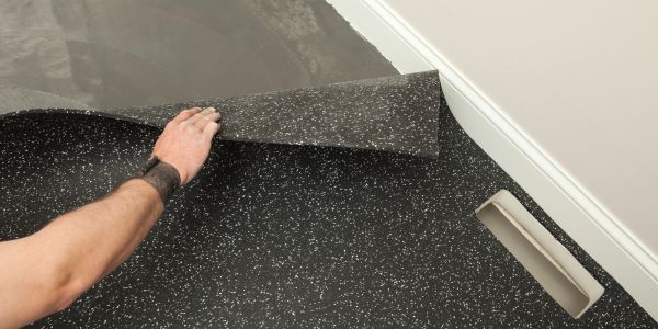 Person installing speckled black rubber flooring in a room.