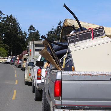 A line of pickup trucks carrying various household items on a sunny day.