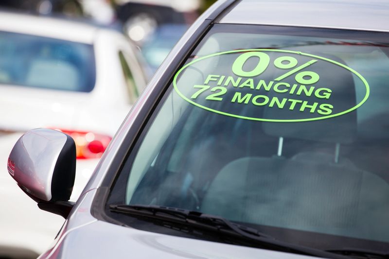 A vehicle at a car dealership displays an advertisement written on the front windshield.  "0% Financing 72 Months".