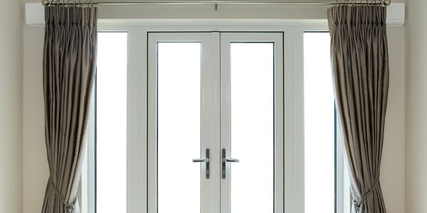 White double doors with beige curtains tied back.