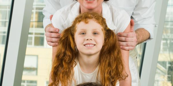 Smiling child with red hair in front of an adult indoors.