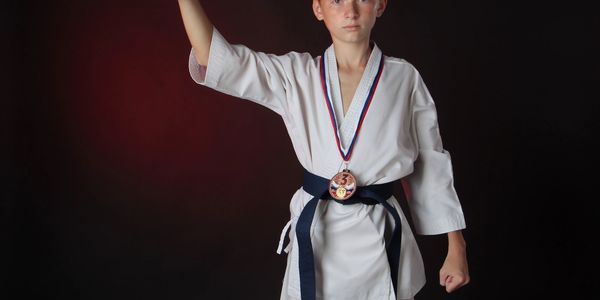 Young martial artist with a bronze medal and black belt posing confidently.