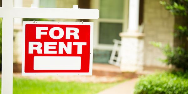 Red and white 'For Rent' sign in front of a house with a porch.