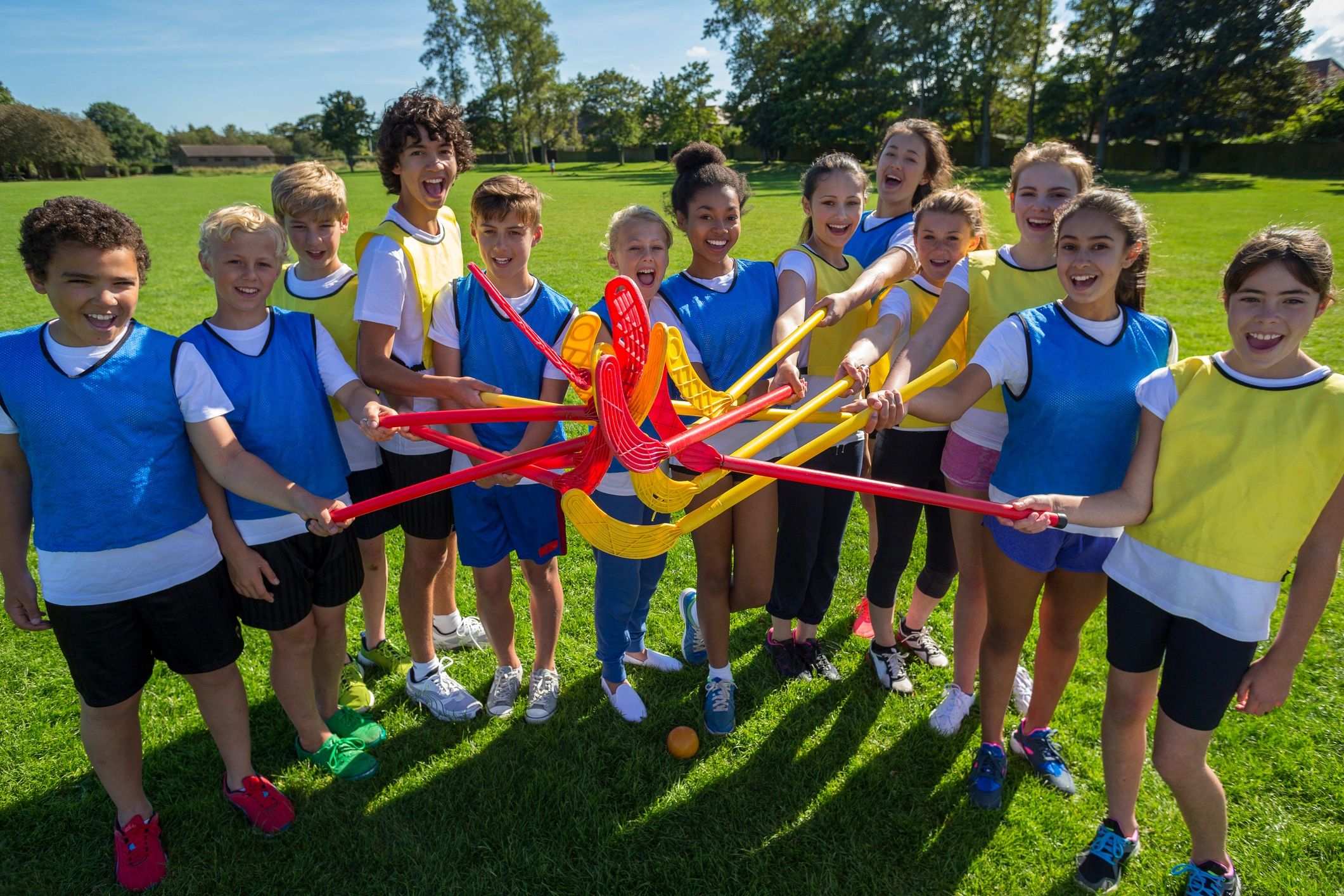 Group of kids holding floorball sticks in a circle outdoors.