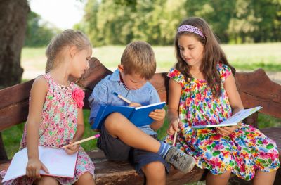 Three children writing and drawing outdoors on a bench.