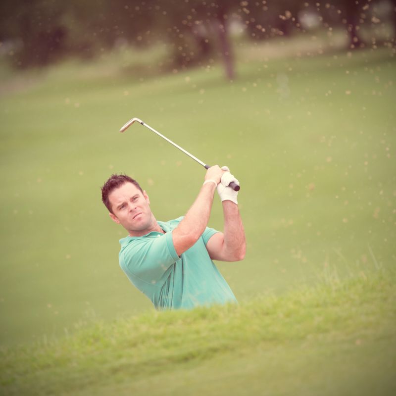 Golfer hitting golf ball out of sand trap on course