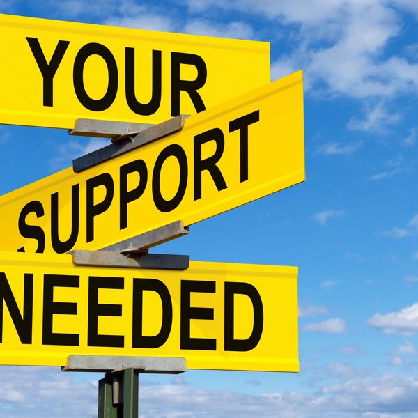 Yellow street signs read 'YOUR SUPPORT NEEDED' against a blue sky.