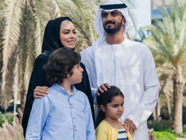 A Middle Eastern family enjoying time outdoors with palm trees in the background.