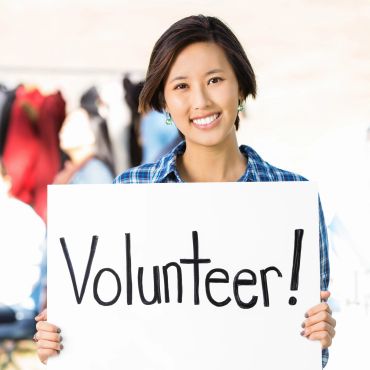 Smiling woman holding a sign that says 'Volunteer!'