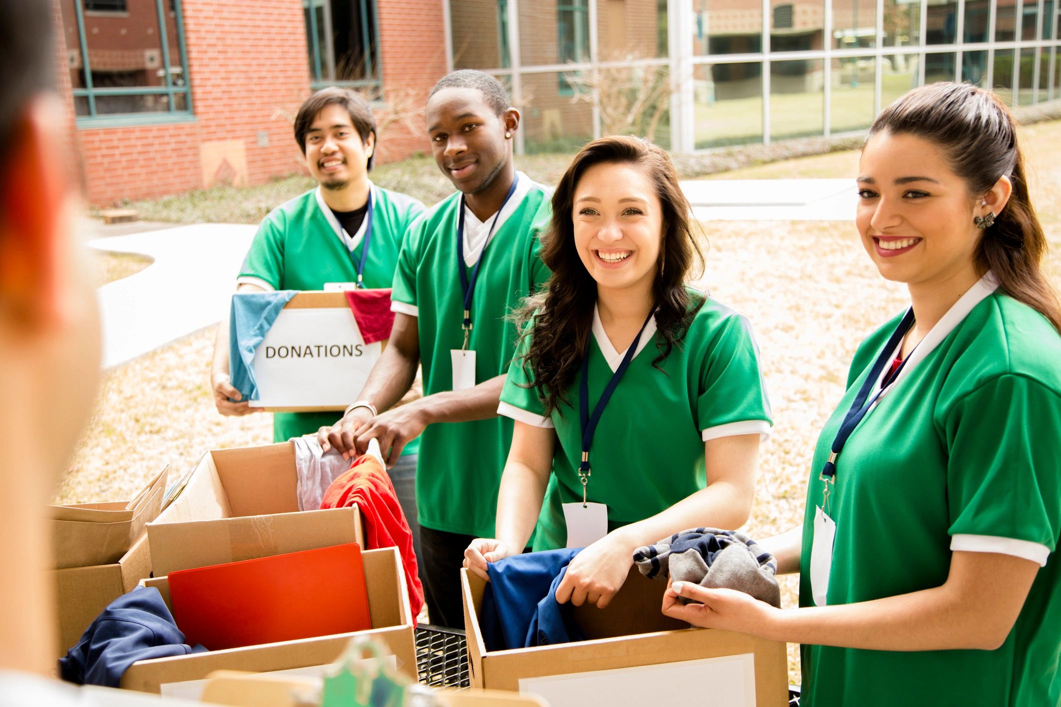 Four volunteers in green shirts collecting clothing donations outdoors.