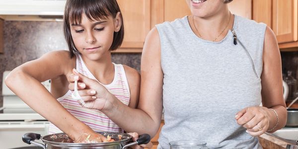 Mother and daughter cooking together, mixing ingredients in a large pot.
