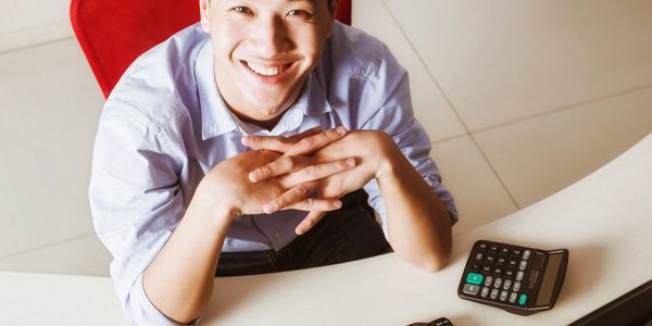 Smiling young man sitting at desk with calculator and keyboard.