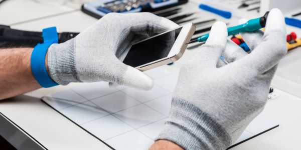Technician repairing a smartphone with gloves and tools.