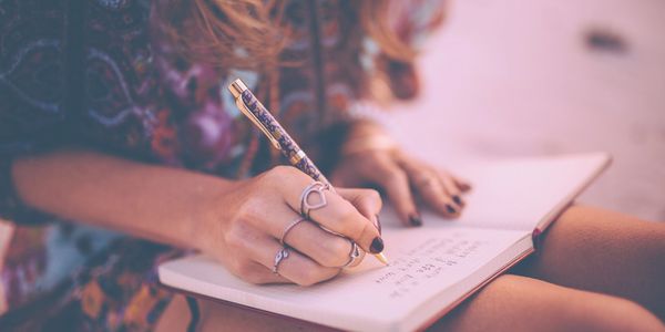 Person writing in a notebook with a decorative pen outdoors.