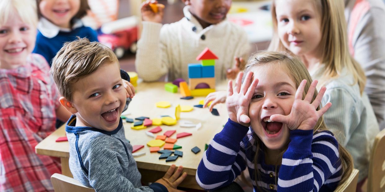 Two women and two toddlers engaging in playful learning activities in a colorful classroom.
