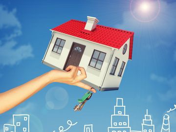 Hand holding a house model with keys against a sunny sky and city sketches.