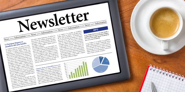 Tablet displaying a newsletter beside a cup of coffee and a notepad on a wooden table.