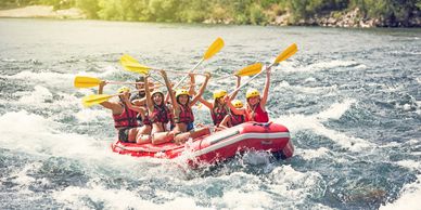 Group enjoying white-water rafting with raised paddles on a sunny day.