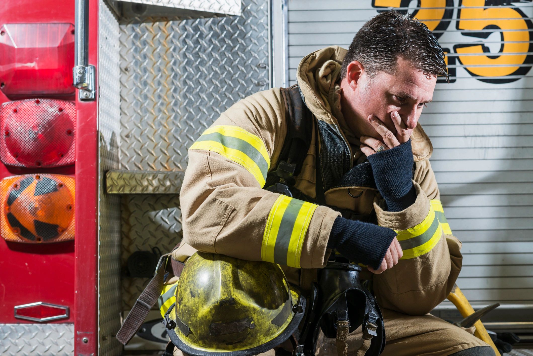 Tired firefighter in uniform sitting by fire truck, deep in thought.