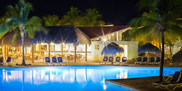 A beautifully lit poolside area at night with palm trees and lounge chairs.