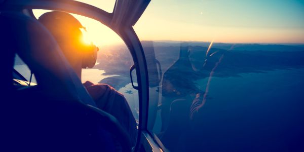 Pilot flying a helicopter during sunset over a scenic landscape.