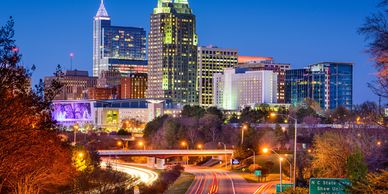 Night view of a city skyline with illuminated buildings and light trails on a highway.