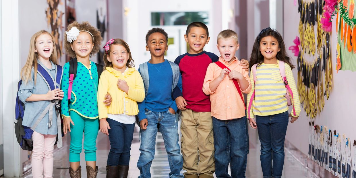 Happy children standing in a school hallway with backpacks.
